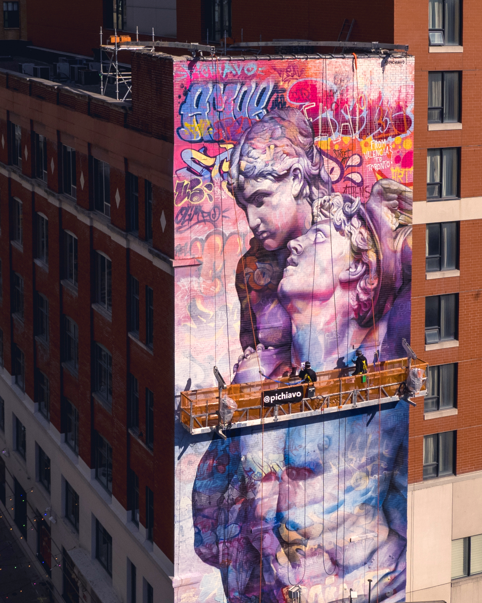 Artist duo PichiAvo on scaffolding, working on a mural of Mercury and Venus in Toronto.