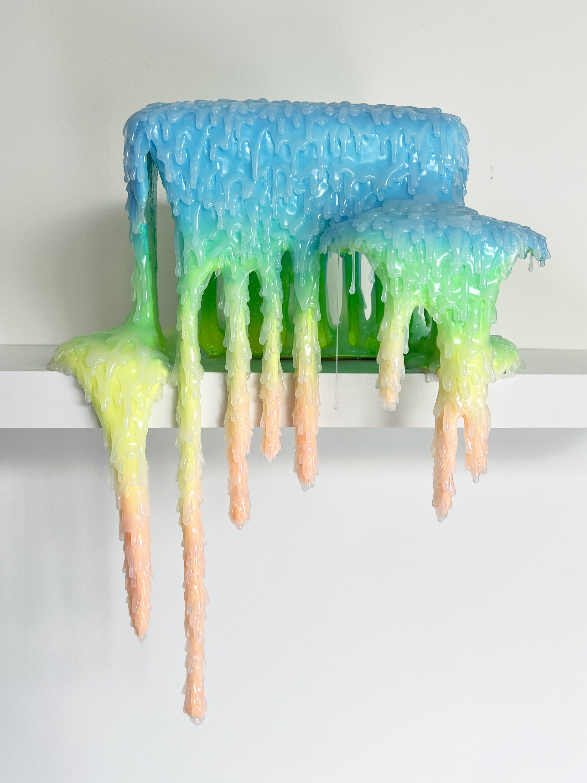 An abstract and colorful sculpture in resin, acrylic and polyurethane foam that seems to ooze on a shelf.