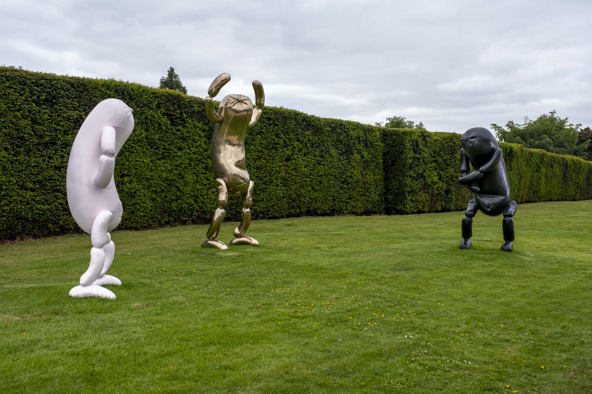 Three sausage sculptures with arms and legs that appear to dance on the lawn.