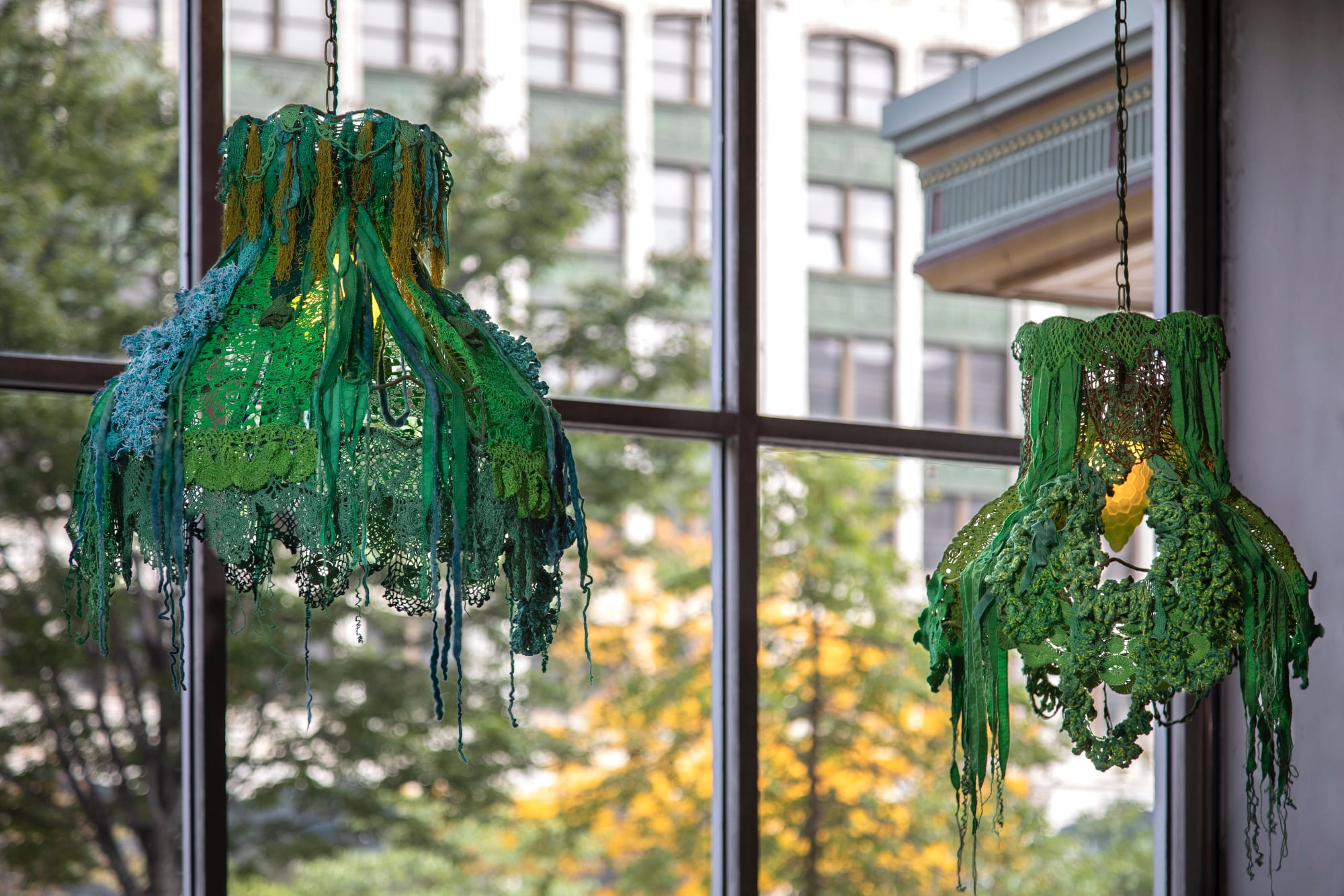 two pendant lights covered in green crochet hang in front of a window