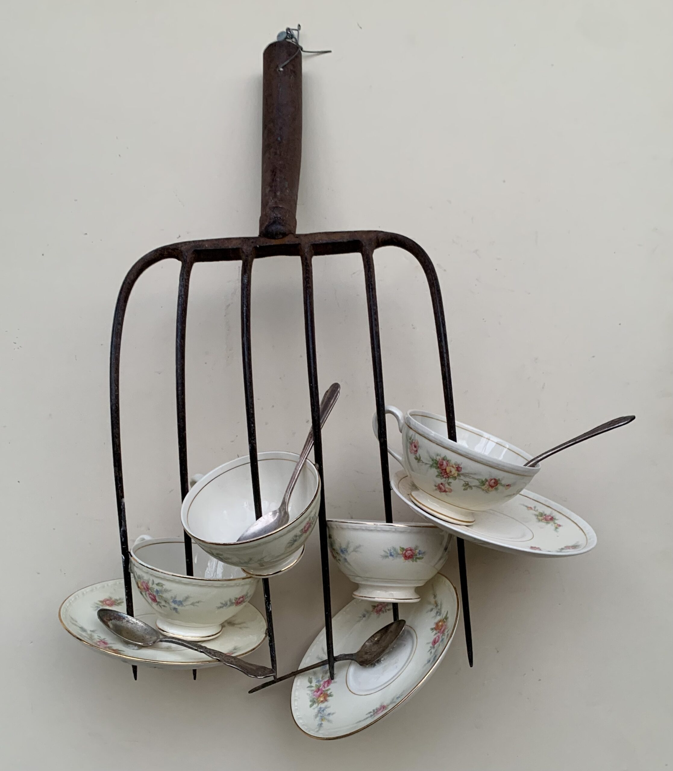 A pitchfork spears a series of teacups and spoons.