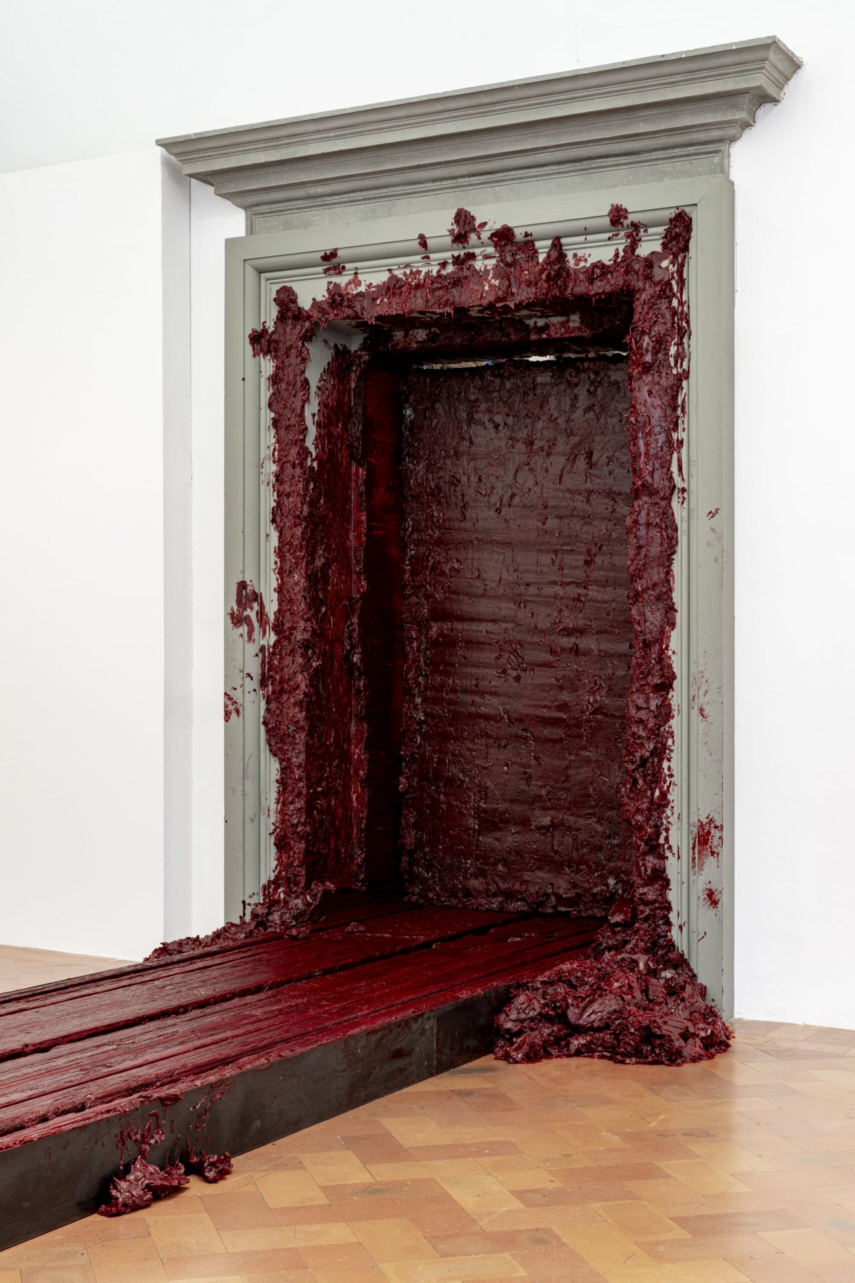 a massive red wax brick pushes through a doorway