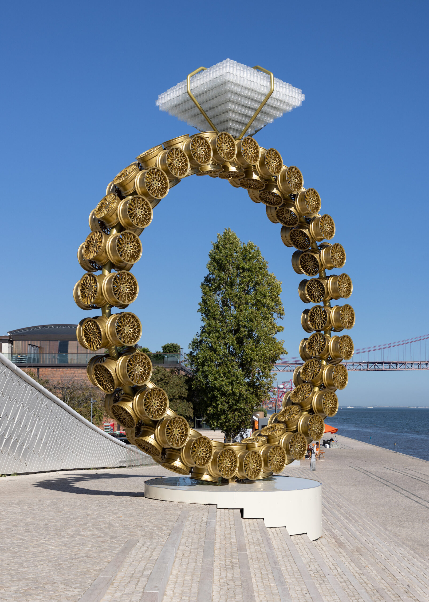 A large sculpture of a diamond ring made out of car wheels and glass.