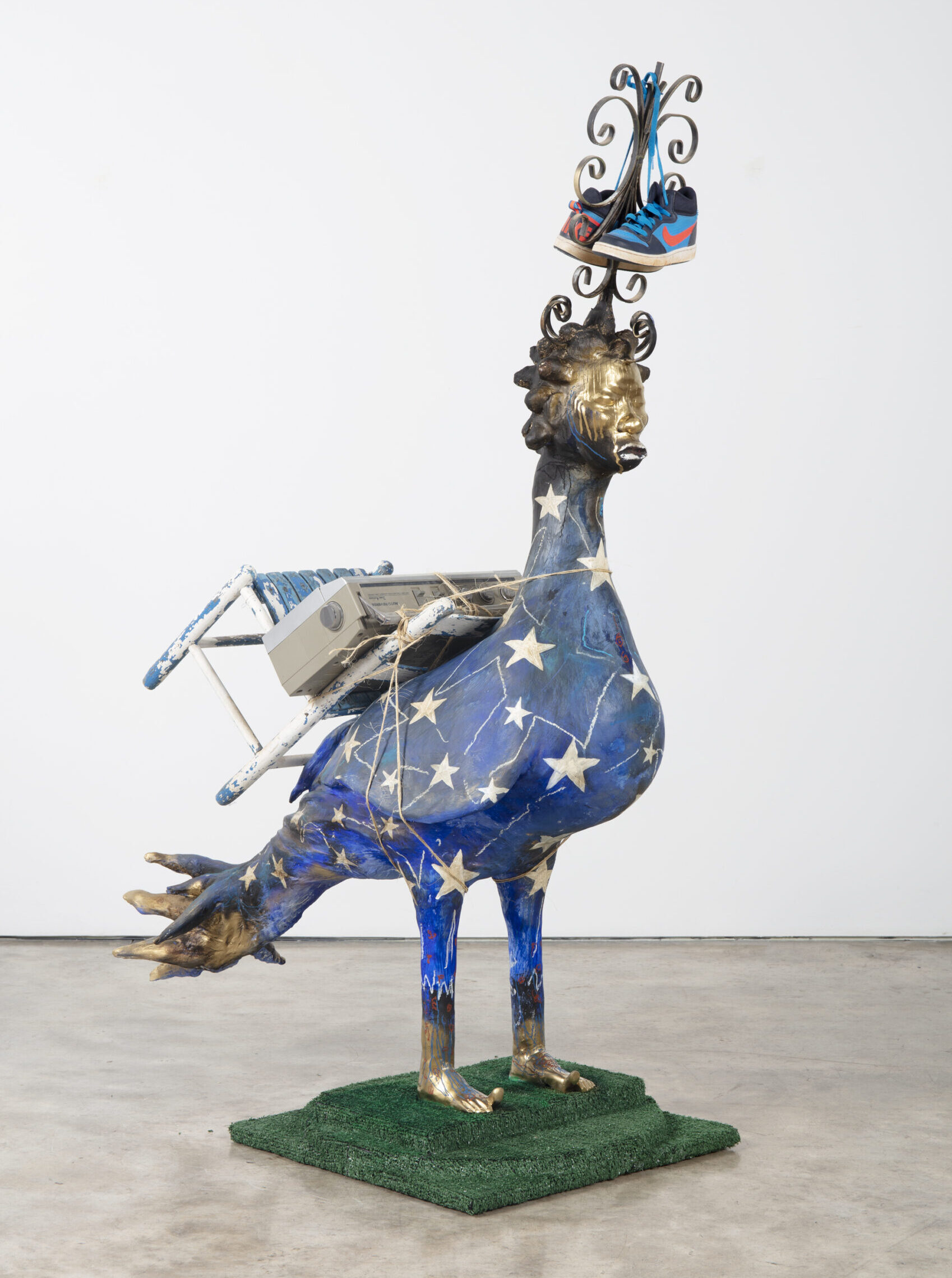 A mixed-media sculpture of a bird-like creature with Nike shoes on its head and a chair with an air conditioner on its back.