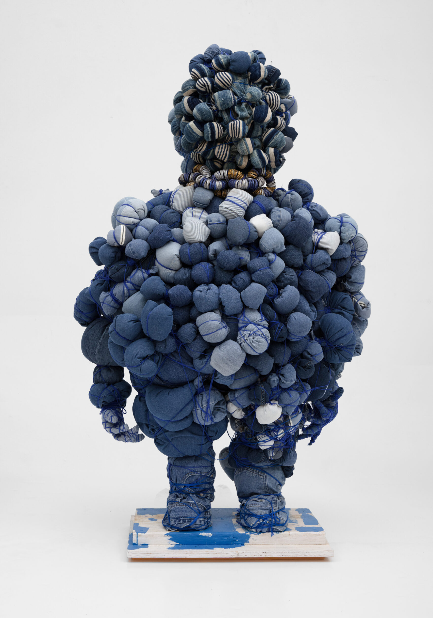 A mixed-media sculpture made of different pairs of blue jeans all balled up with yarn and twine.