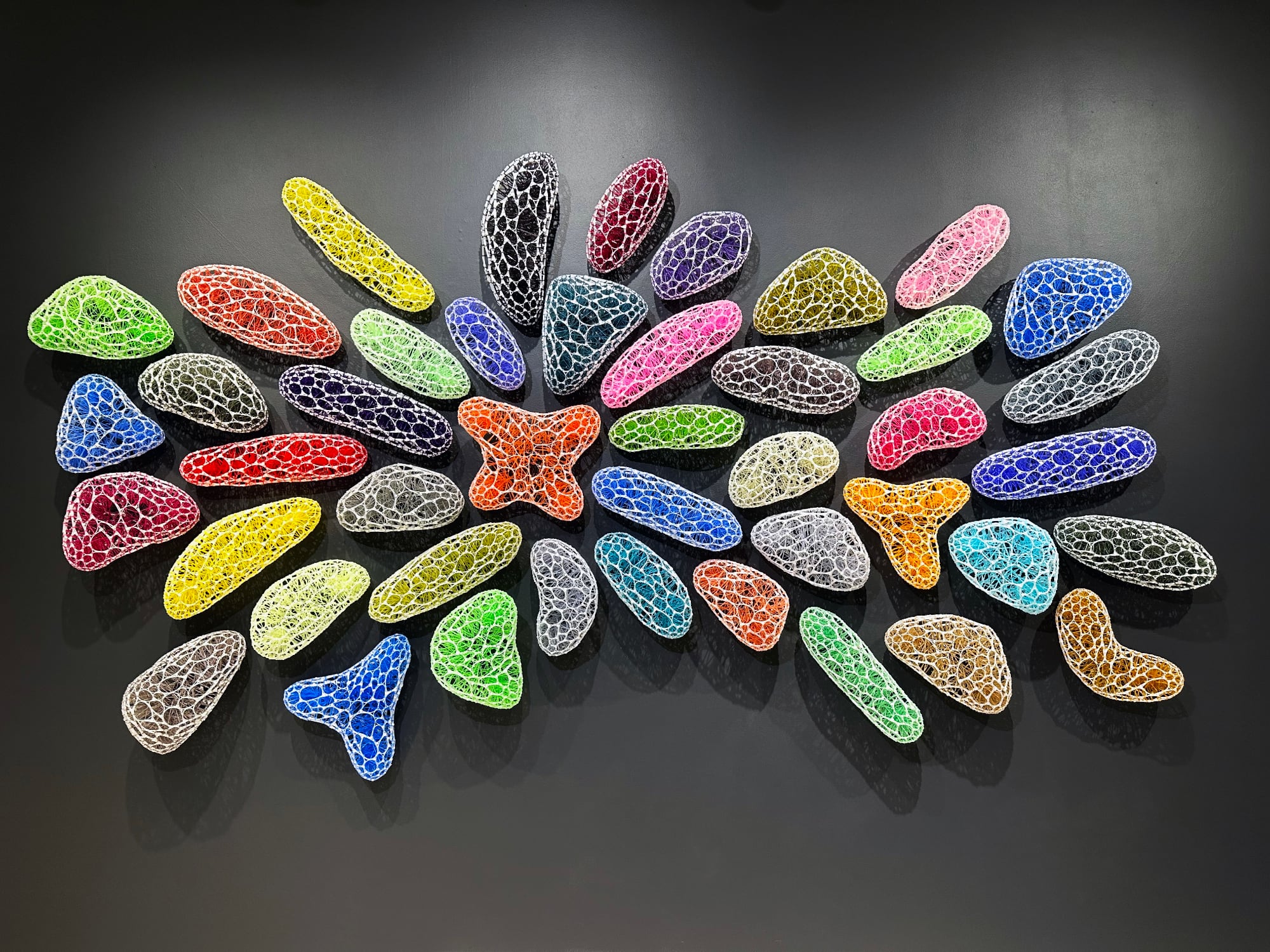 a collection of small colorful sculptures in a cluster on a gray wall