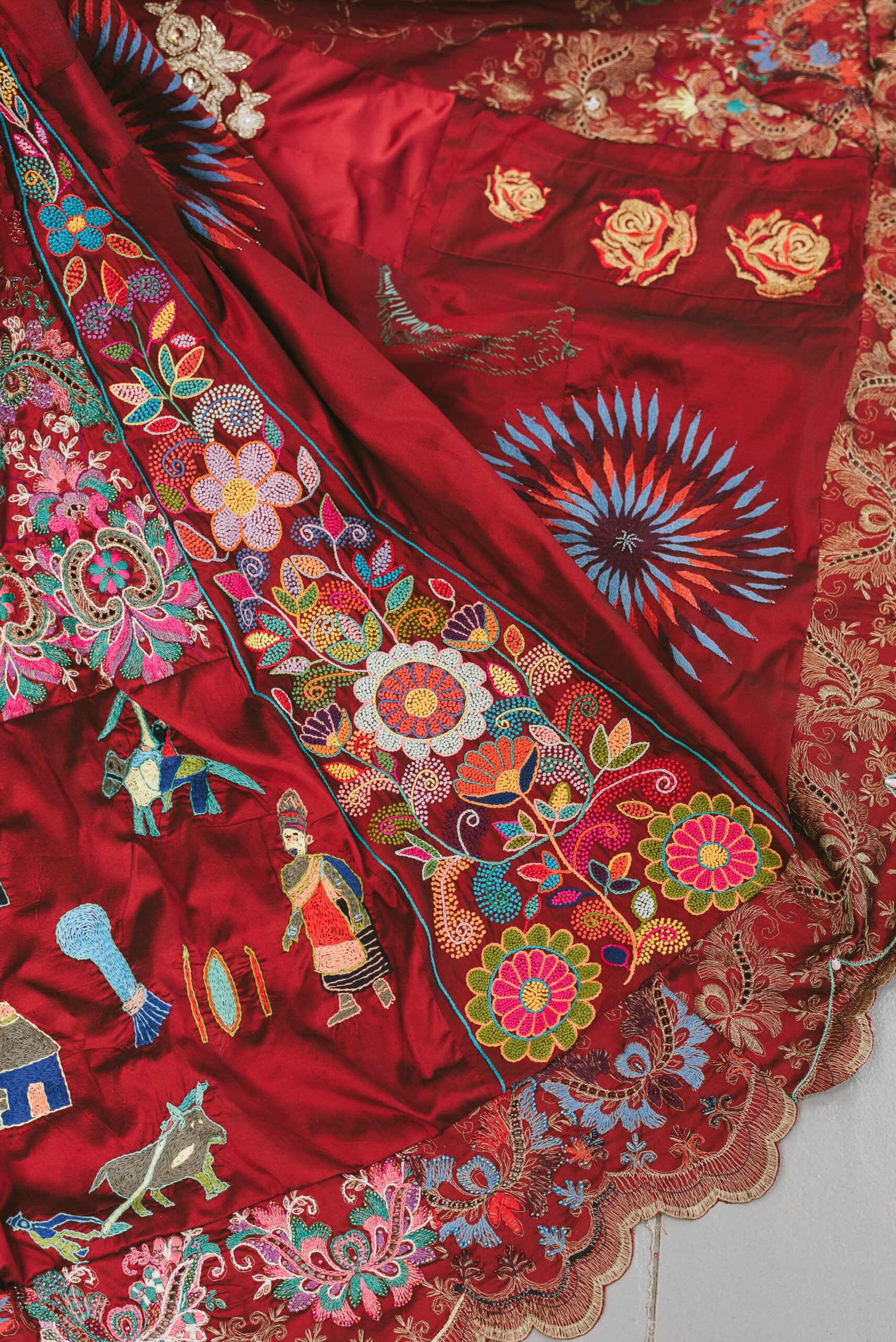 a detail of floral, figurative, and patterned embroideries on a red dress