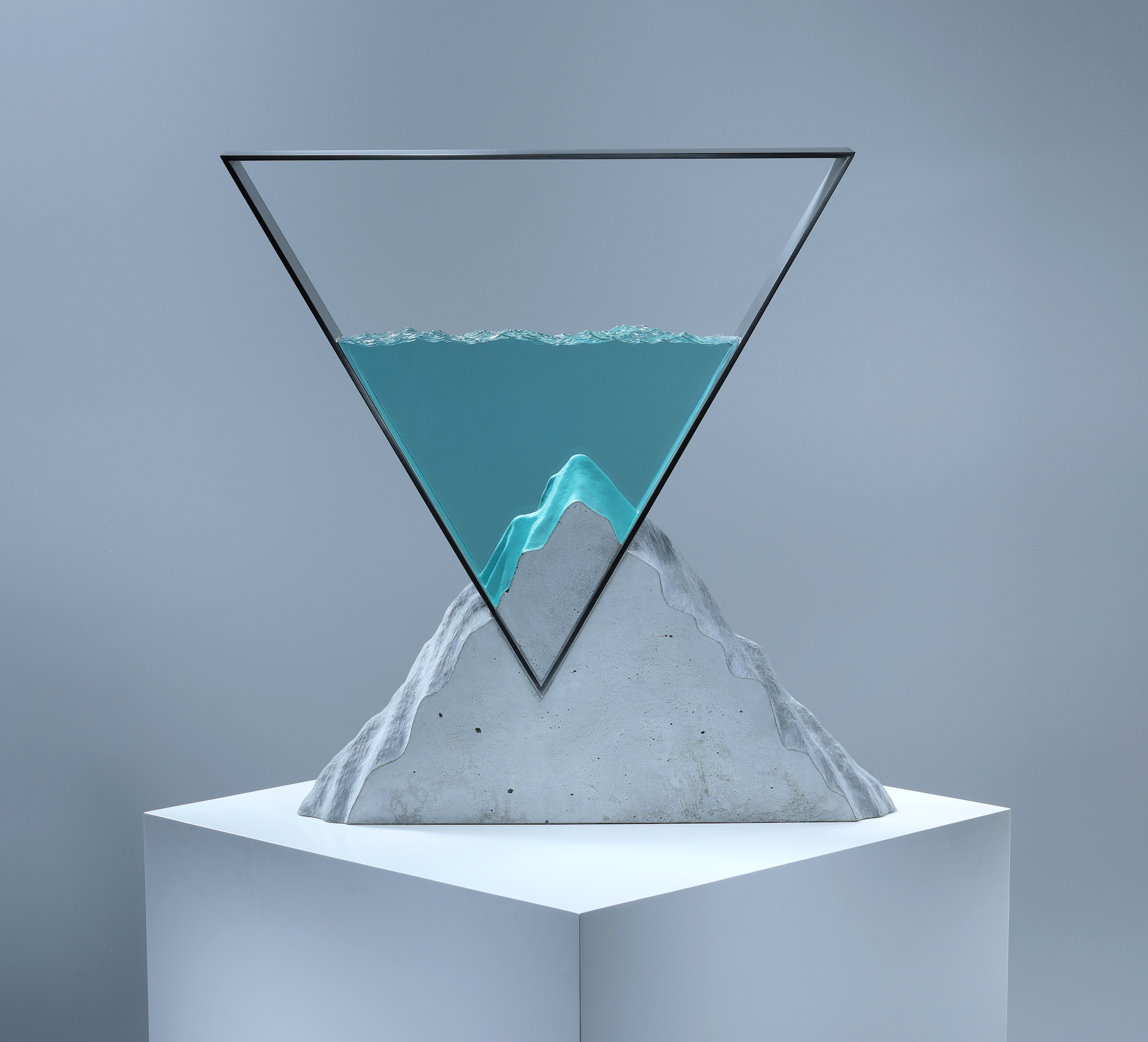 A triangular metal frame containing layers of glass resembling water, which is inverted into a triangular slab of concrete that resembles a mountain.