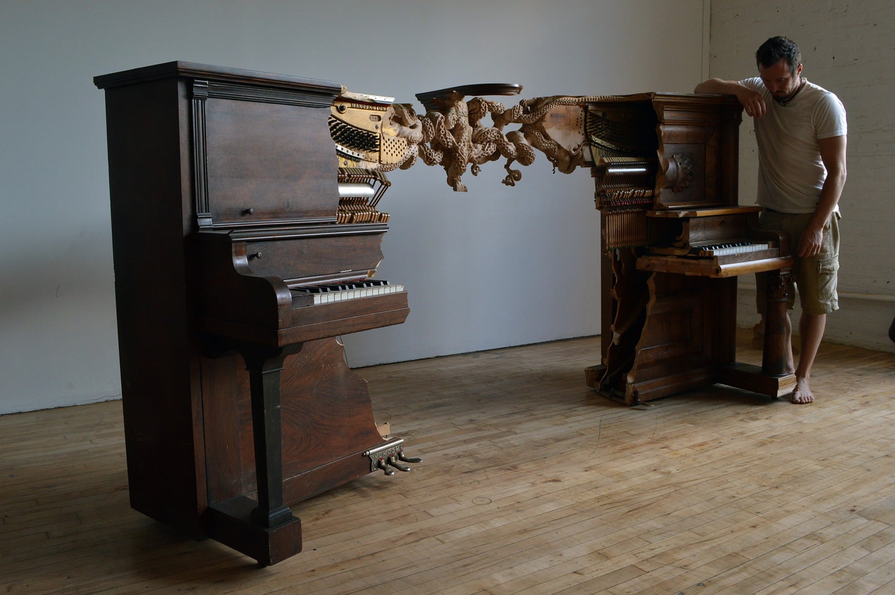 the artist rests his arm on a sculpture of two pianos sliced and connected by a carved knotted octopus