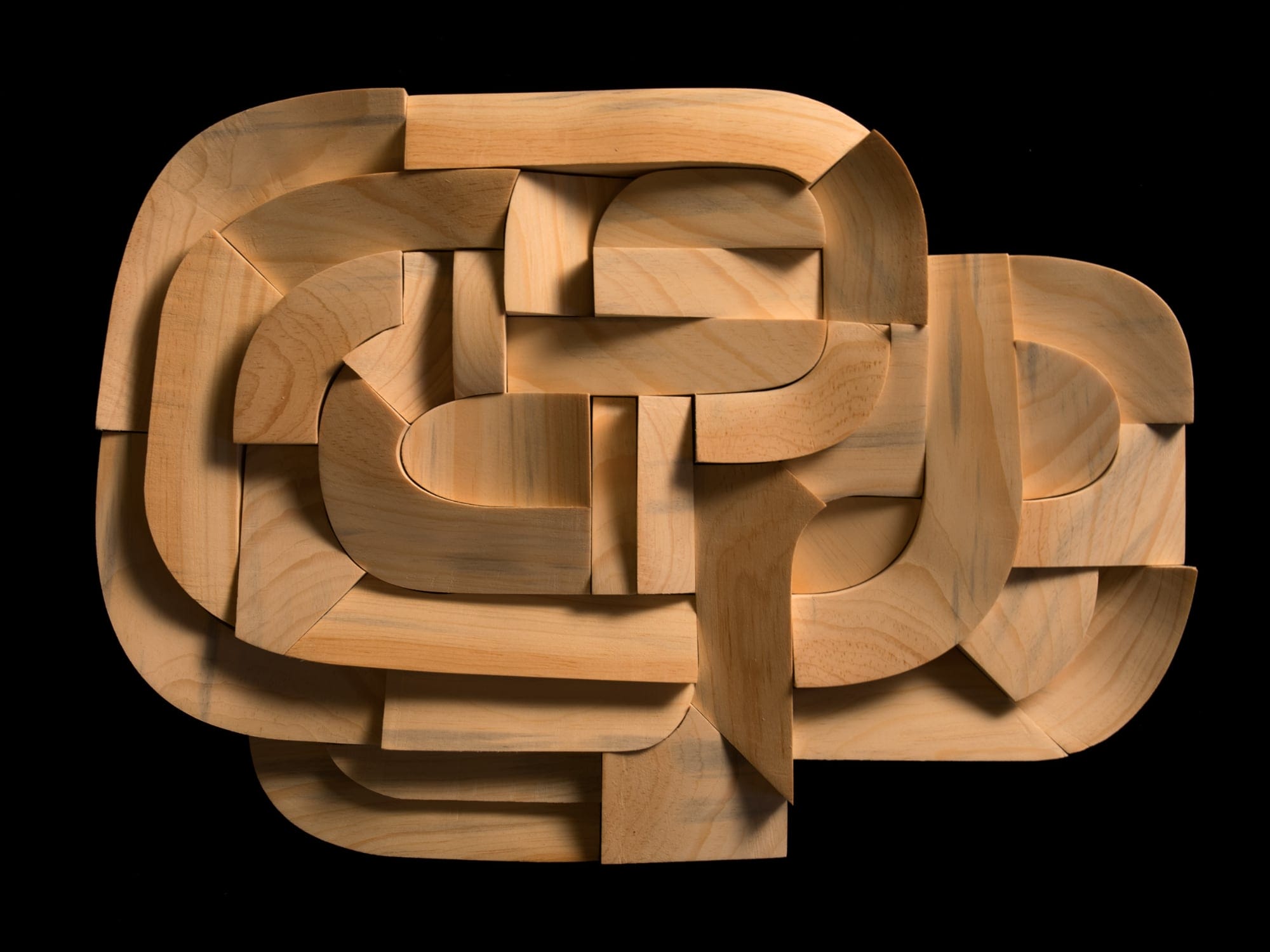 an oval wooden sculpture with fragmented pieces on various levels against a black backdrop